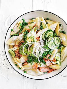 a bowl filled with pasta and vegetables on top of a white table next to a fork