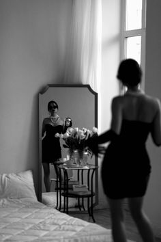 a woman standing in front of a mirror next to a bed