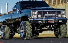 a large black truck parked on top of a parking lot next to a tall building