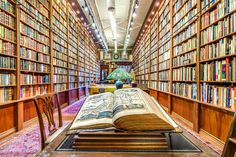 an open book sitting on top of a wooden table in a library filled with books