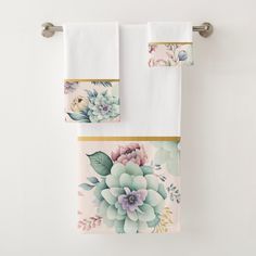 two white towels hanging on a towel rack with flowers and leaves painted on the front