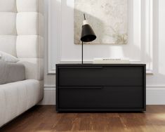 a black nightstand with a lamp on it in front of a white couch and window