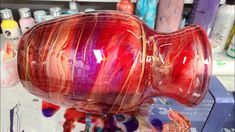 a red glass vase sitting on top of a table next to other paint and brushes