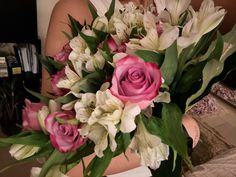 a woman holding a bouquet of pink and white flowers in her hands on the bed