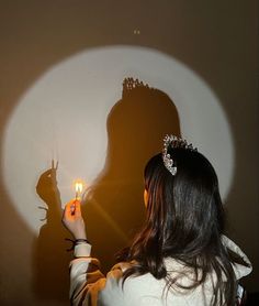 a woman holding a candle in front of a wall with a shadow on the wall behind her