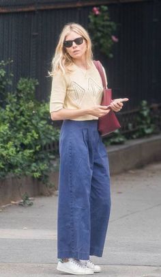 a blonde woman in blue pants is looking at her cell phone