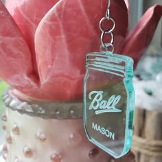 a mason jar with pink flowers in it hanging from a chain that is attached to a vase