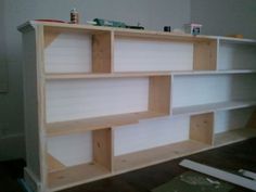 an unfinished bookcase is being built with plywood and white paint on the walls