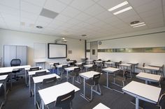 an empty classroom with desks and whiteboards on the wall, in front of a projector screen