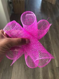 a hand holding a pink mesh flower on top of a hard wood floor in a living room