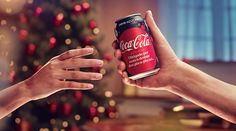 two people reaching out their hands to each other with a can of coca - cola in front of a christmas tree