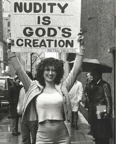 a woman holding up a sign that says nudety is god's creation