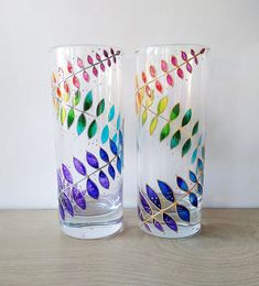 two colorful glasses sitting on top of a wooden table