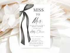 a black and white wedding card with a ribbon on it, next to some flowers