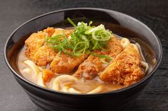 a black bowl filled with noodles and meat covered in gravy, garnished with scallions