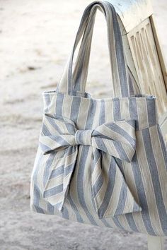 a gray and white striped bag with a bow on the front sitting on a wooden bench