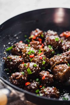 meatballs are cooked in a wok with green onions and carrots on the side