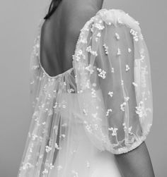 the back of a woman's dress with white flowers on it and sheer sleeves