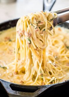 a fork full of spaghetti being lifted from a skillet with the noodles in it