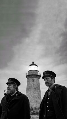 two men standing next to each other in front of a light house