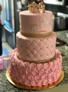 a three tiered cake with pink roses and a gold crown on top is sitting on a counter