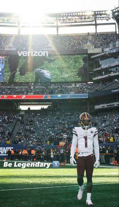 a football player standing on the field in front of a large screen at a stadium