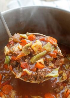 a ladle full of stew with carrots and celery in it is being held by a spoon