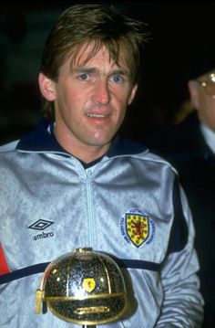 a man holding a soccer ball in his hand and wearing a silver jacket with yellow trim