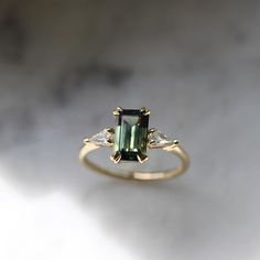 an emerald and diamond ring sitting on top of a table