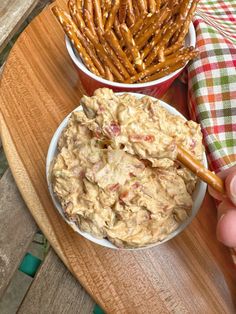 a person holding a wooden spoon in front of two bowls of dip and pretzels