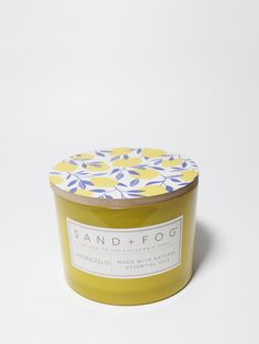 a yellow candle with blue and white flowers on the lid sits in front of a white background