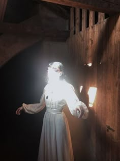 a woman in a white dress standing next to a wooden wall with light coming through her eyes