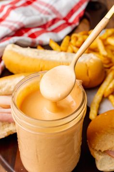 a wooden plate topped with hot dogs and french fries next to a jar of peanut butter