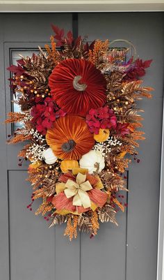 a wreath with red, orange and yellow flowers hanging on the front door for fall