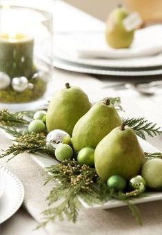 the table is set with green fruit and greenery on it, including pears