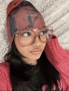 a woman wearing glasses and a knitted hat is laying on a white blanket looking at the camera