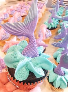 cupcakes with blue and purple frosting are being held by someone's hand