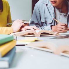 two people sitting at a table with books and pencils in their hands while one person writes