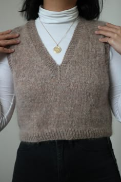 a woman wearing a sweater vest with a gold heart pendant on it's neck