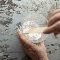 a hand holding a spoon over a bowl filled with flour