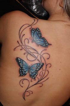 the back of a woman's shoulder with two blue butterflies on it and swirls