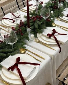 the table is set with white plates, silverware and greenery for christmas dinner