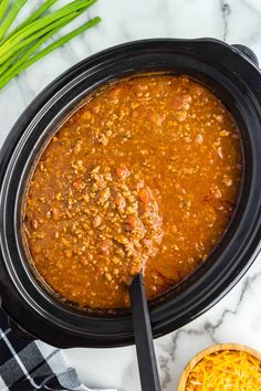 a crock pot filled with chili and cheese next to a bowl of shredded cheese