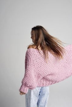 a woman with her hair in the wind wearing a pink knitted sweater and jeans