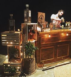 a man standing behind a bar filled with liquor bottles and other items on top of it