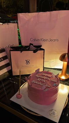 a pink cake sitting on top of a table next to shopping bags and a lamp