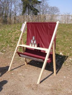 a red chair sitting on top of a dirt field next to a wooden structure with bottles in it