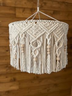 a white crocheted chandelier hanging from a wooden wall with wood beads