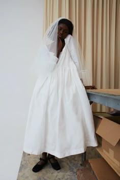 a woman in a white dress and veil standing next to a table with boxes on it