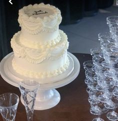 a white wedding cake sitting on top of a table next to wine goblets